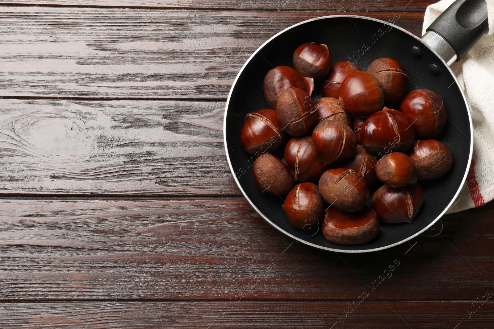 Photo of Roasted edible sweet chestnuts in frying pan on wooden table, top view. Space for text