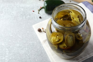 Photo of Glass jar with slices of pickled green jalapeno peppers on light grey table, space for text