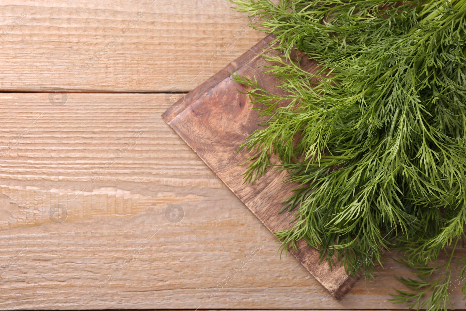 Photo of Board with sprigs of fresh dill on wooden table, top view. Space for text