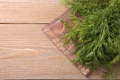 Board with sprigs of fresh dill on wooden table, top view. Space for text