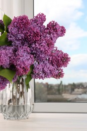 Beautiful lilac flowers in vase on white wooden table indoors, space for text