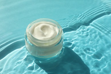 Photo of Jar with moisturizing cream in water on light blue background