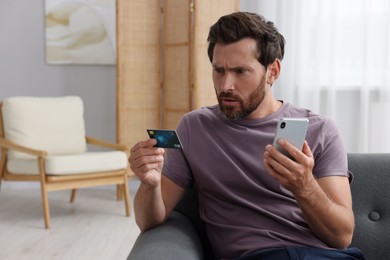 Man with credit card and smartphone on sofa at home, space for text. Be careful - fraud