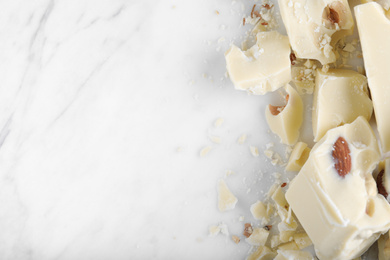 Pieces of white chocolate with nuts on marble table, flat lay. Space for text