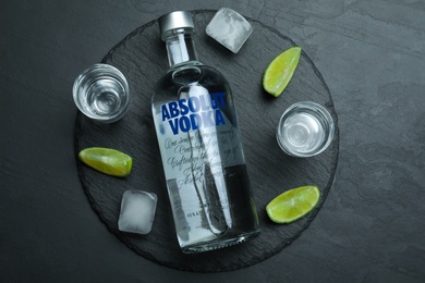 MYKOLAIV, UKRAINE - OCTOBER 04, 2019: Absolut vodka, lime, ice cubes and shot glasses on black table, flat lay