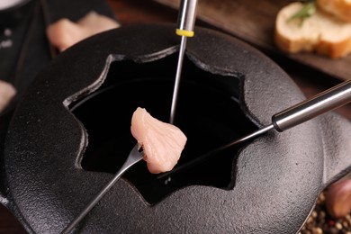 Photo of Fondue pot, forks and piece of raw meat on table, closeup