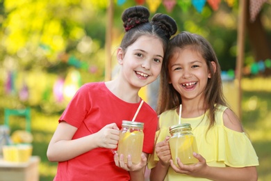 Photo of Cute little girls with natural lemonade in park. Summer refreshing drink