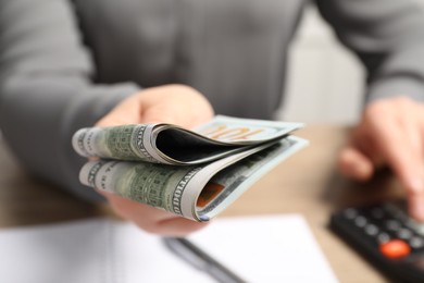 Photo of Money exchange. Woman holding dollar banknotes at wooden table, closeup