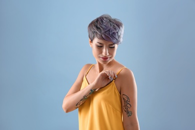 Young woman with tattoos on color background