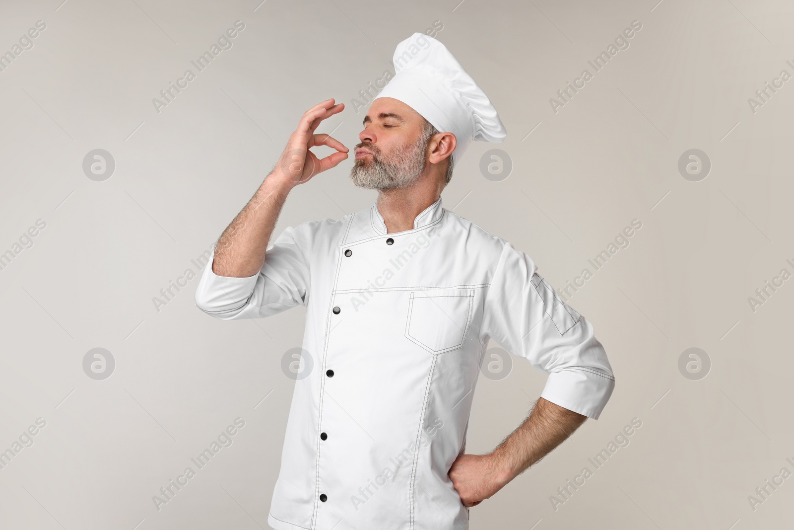 Photo of Chef in uniform showing perfect sign on grey background