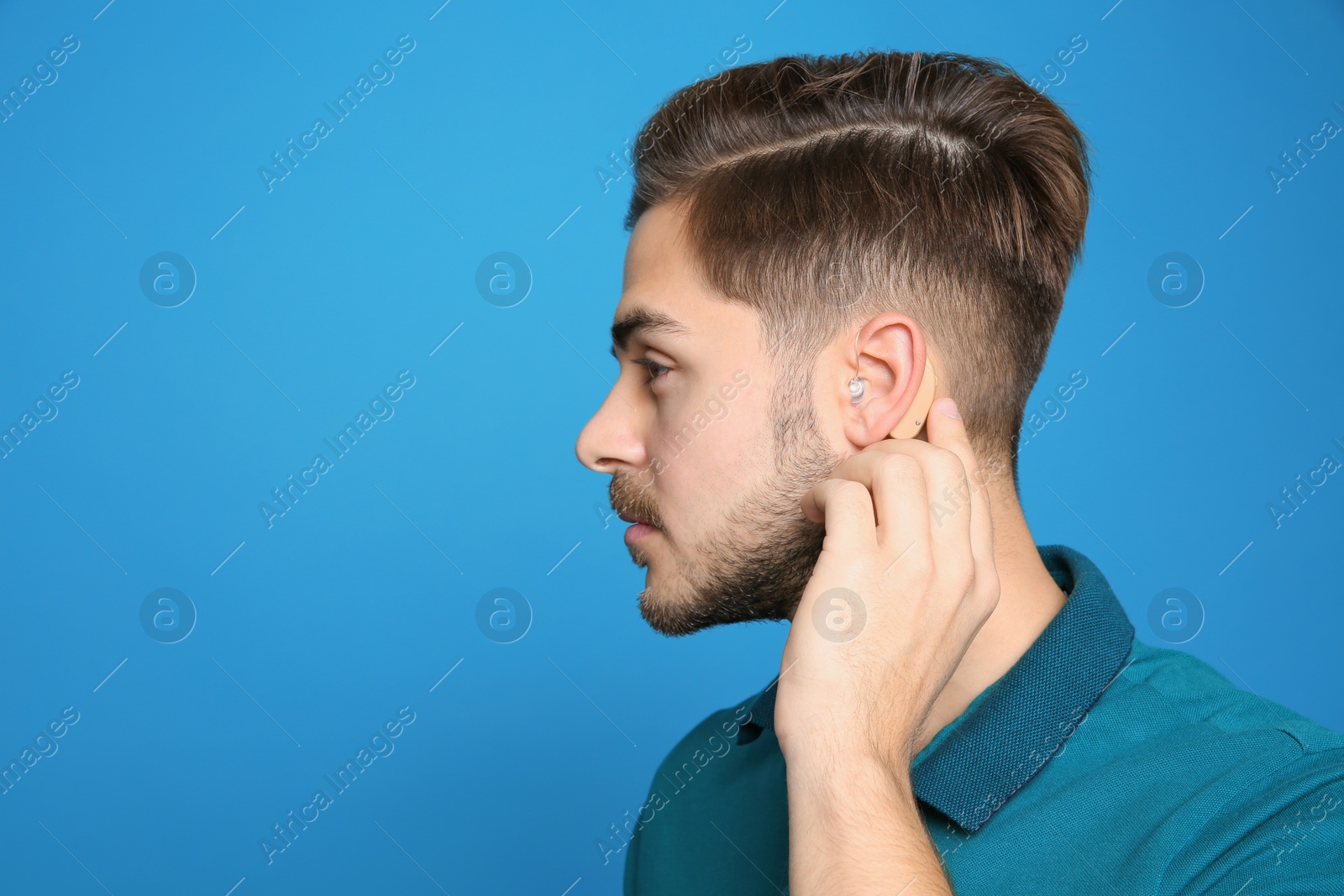 Photo of Young man adjusting hearing aid on color background. Space for text