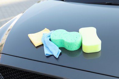 Photo of Sponges and rags on car hood outdoors. Cleaning products