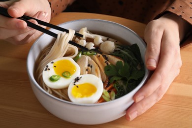 Photo of Woman eating delicious ramen with chopsticks at wooden table, closeup. Noodle soup