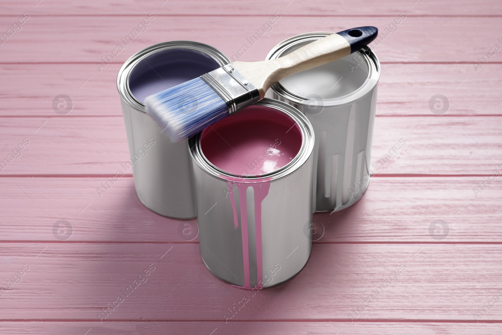 Photo of Cans of pastel paints and brush on pink wooden table