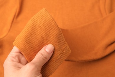 Photo of Woman holding sleeve of orange sweater with lint as background, top view. Before using fabric shaver