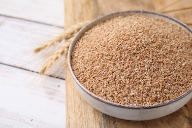 Photo of Dry wheat groats in bowl on white wooden table, closeup. Space for text