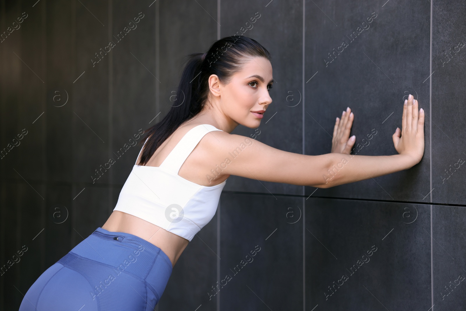 Photo of Beautiful woman in sportswear training near dark grey wall outdoors