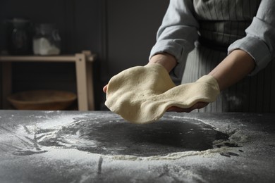 Woman tossing pizza dough at table in kitchen, closeup