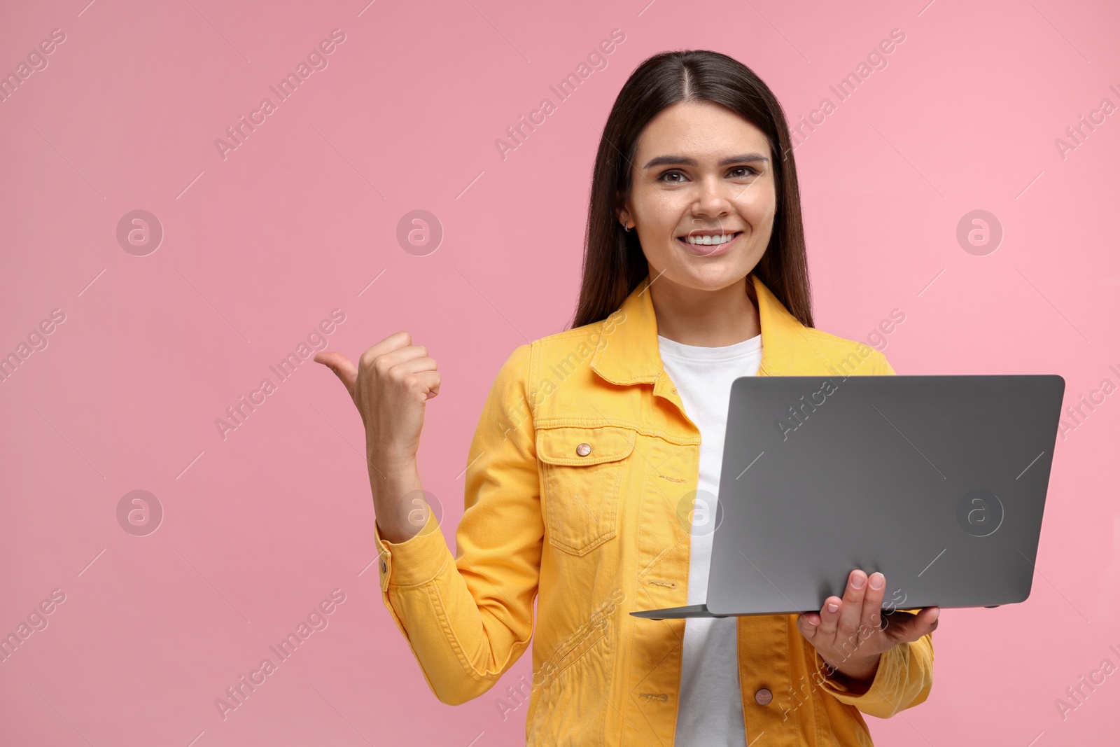 Photo of Special promotion. Happy woman with laptop pointing at something on pink background, space for text