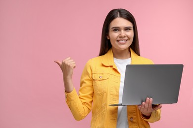 Special promotion. Happy woman with laptop pointing at something on pink background, space for text