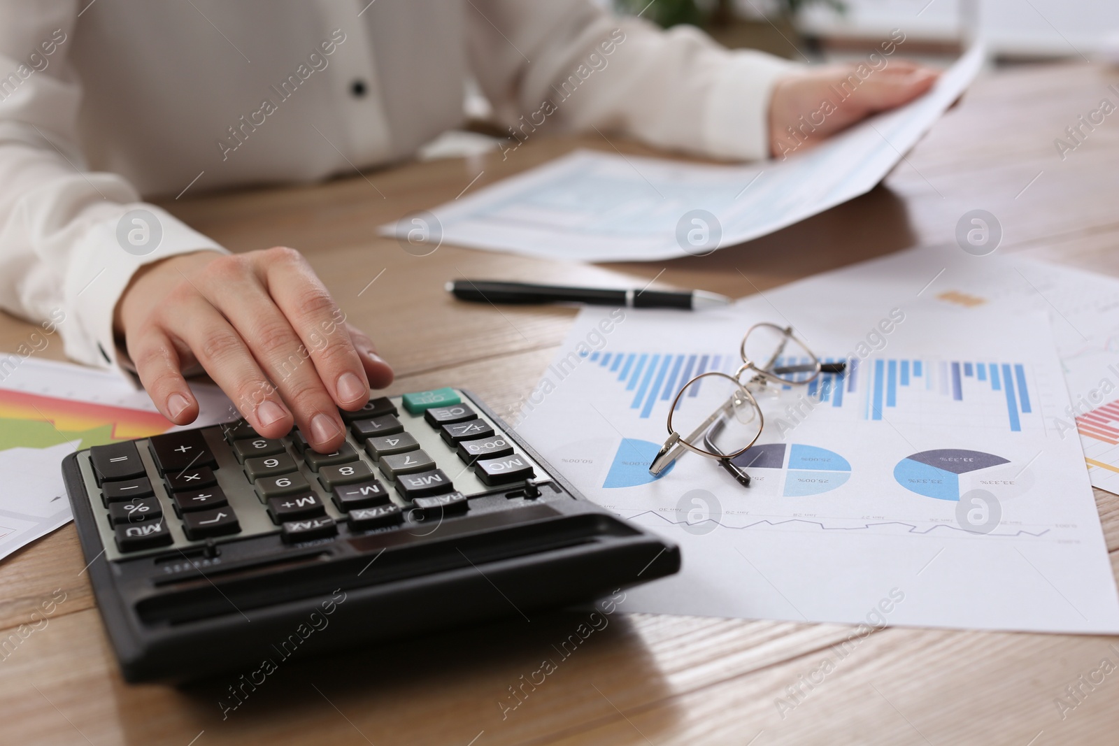 Photo of Tax accountant with calculator working at wooden table, closeup