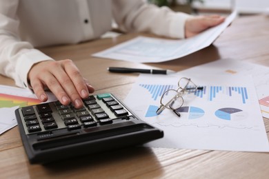 Photo of Tax accountant with calculator working at wooden table, closeup