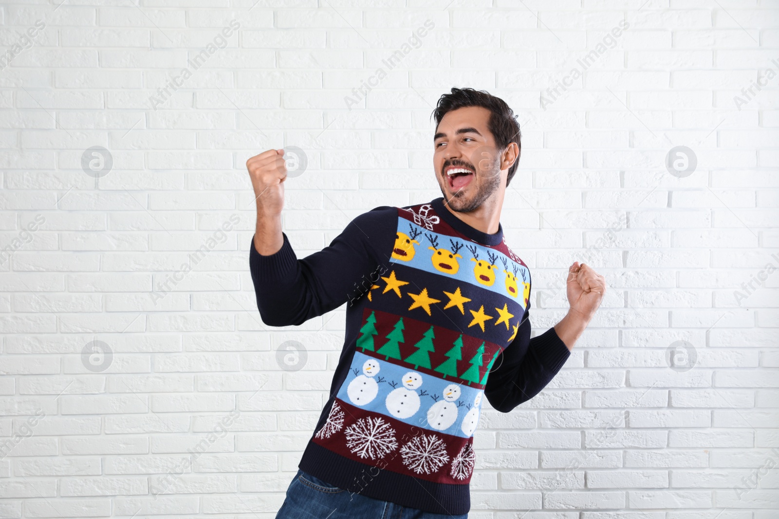 Photo of Emotional young man in Christmas sweater near white brick wall