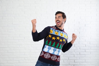 Photo of Emotional young man in Christmas sweater near white brick wall