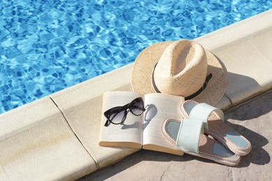 Stylish sunglasses, slippers, straw hat and book at poolside on sunny day. Beach accessories