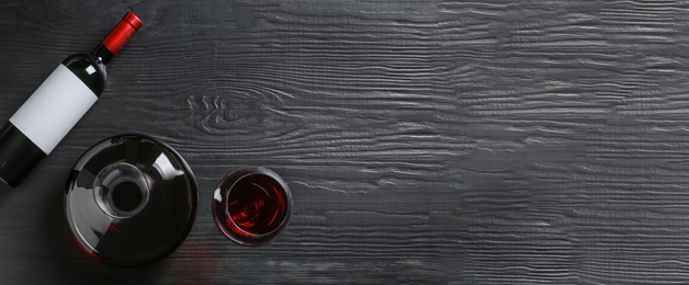 Decanter, glass and bottle with red wine on wooden background, top view. Banner design