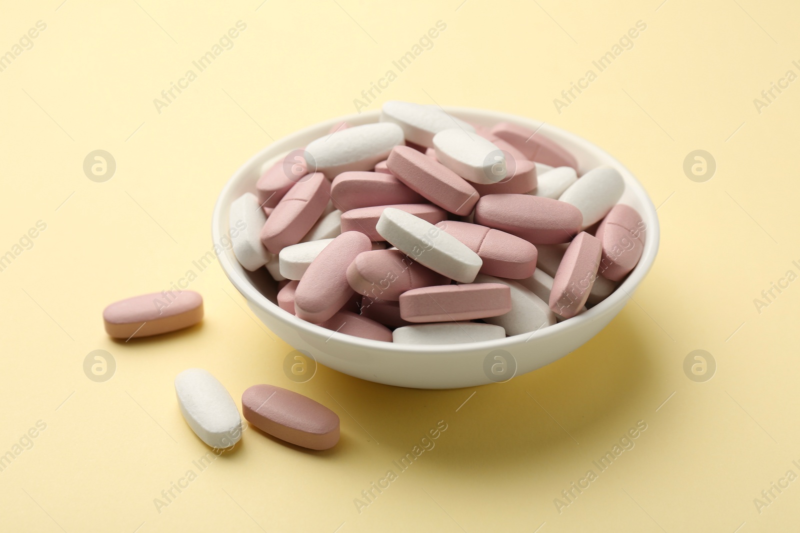 Photo of Different vitamin pills in bowl on pale yellow background