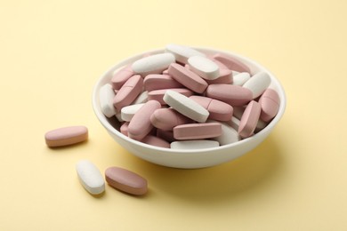 Different vitamin pills in bowl on pale yellow background