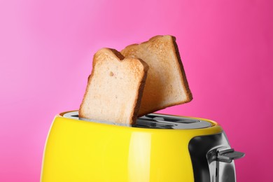 Yellow toaster with roasted bread against pink background, closeup