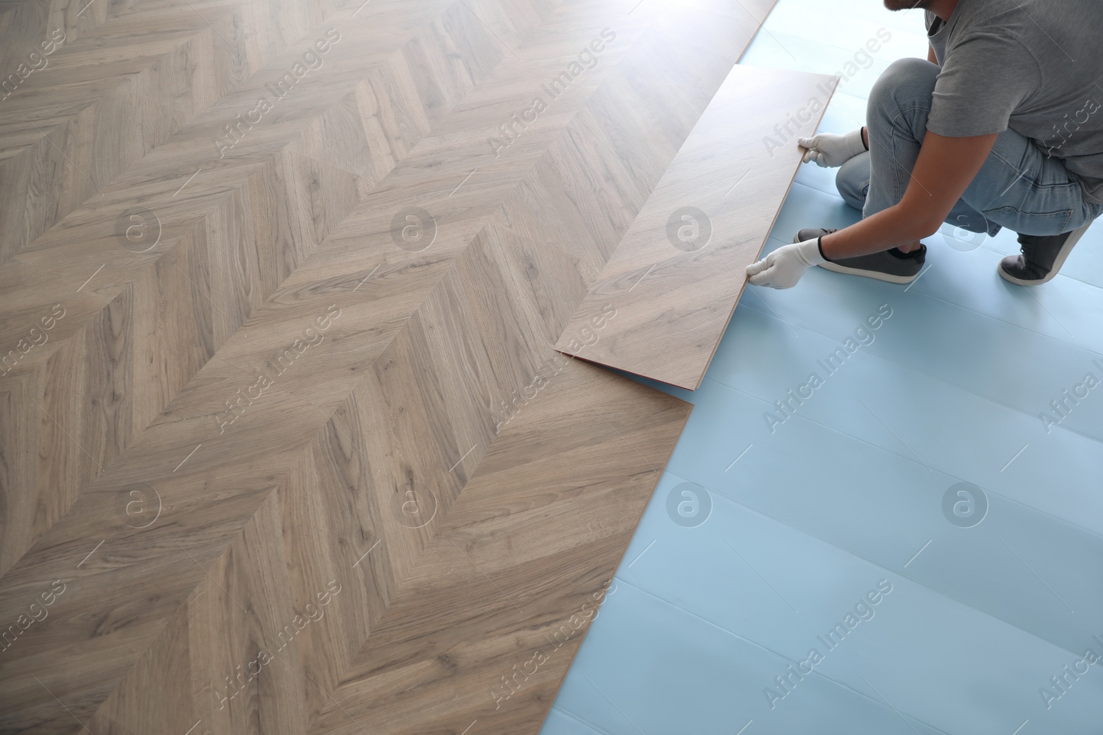 Photo of Worker installing laminated wooden floor indoors, closeup