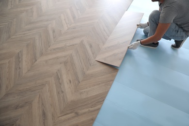 Photo of Worker installing laminated wooden floor indoors, closeup