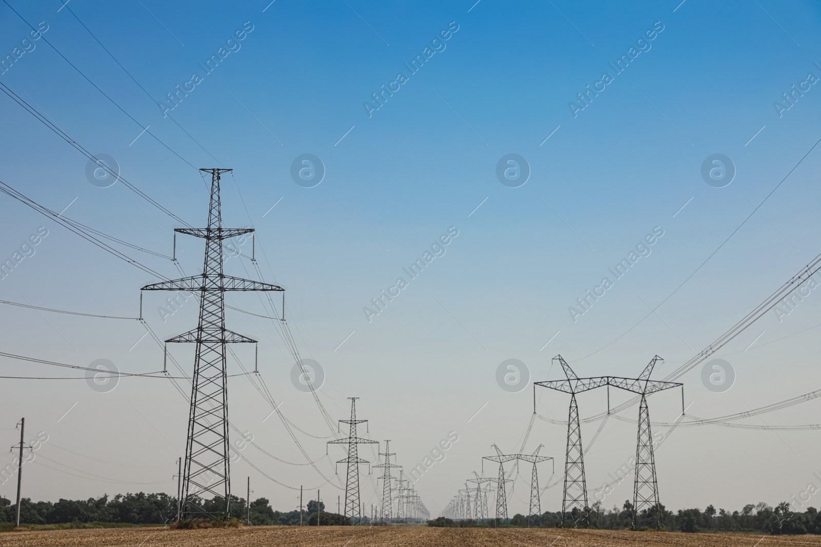 Photo of High voltage towers with electricity transmission power lines in field on sunny day