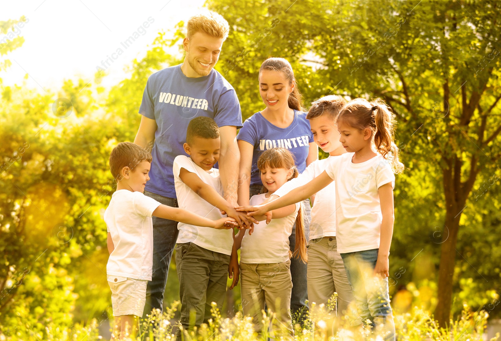 Image of Group of kids joining hands with volunteers in park on sunny day