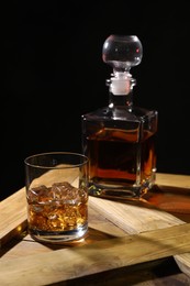 Whiskey with ice cubes in glass and bottle on wooden crate against black background