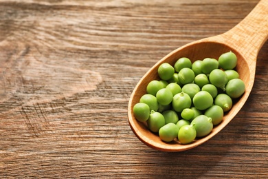 Photo of Spoon with green peas on wooden background, closeup