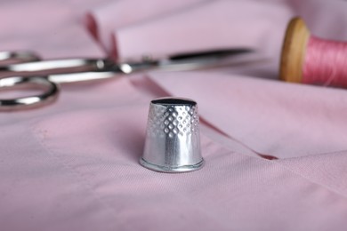 Silver thimble on pink cloth, closeup. Sewing accessory