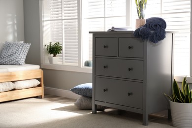 Grey chest of drawers near window in stylish bedroom interior