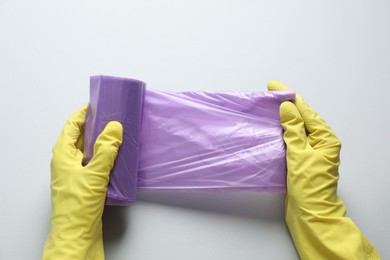 Photo of Janitor in rubber gloves holding roll of violet garbage bags over light background, top view