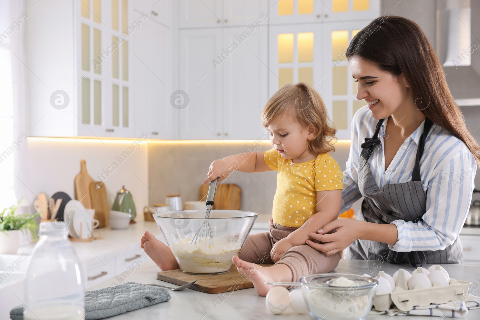 Photo of Mother and her little daughter cooking dough together in kitchen