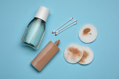 Bottle of makeup remover, foundation, buds and dirty cotton pads on light blue background, flat lay