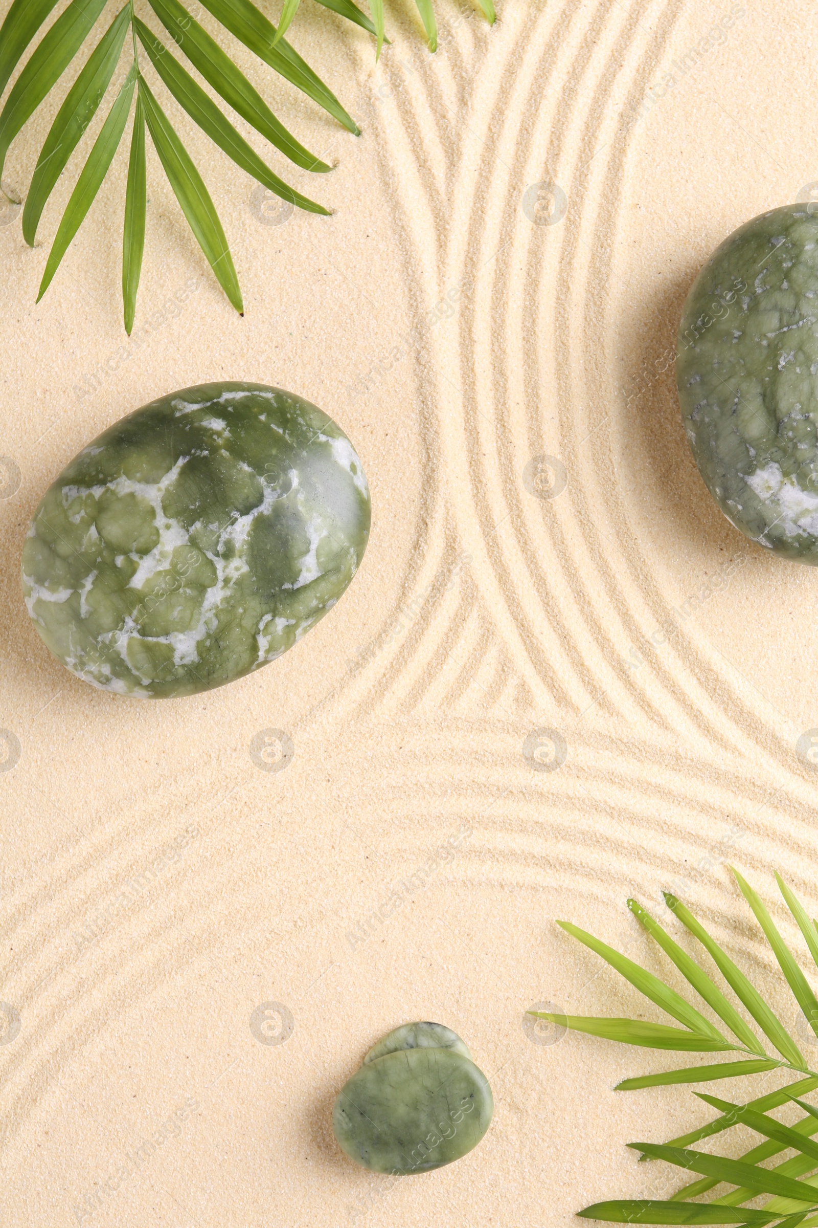 Photo of Zen concept. Stones, leaves and pattern on beige sand, flat lay