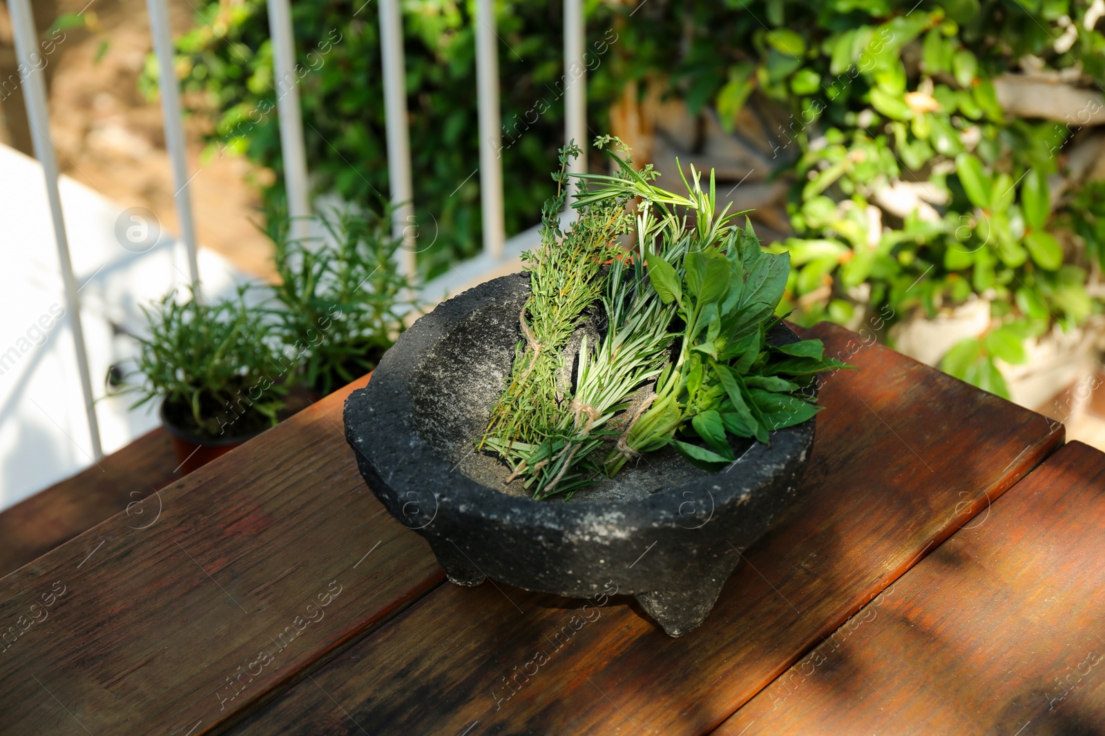 Photo of Mortar with thyme, rosemary and basil on wooden table outdoors. Aromatic herbs