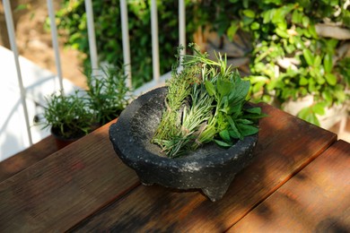 Photo of Mortar with thyme, rosemary and basil on wooden table outdoors. Aromatic herbs