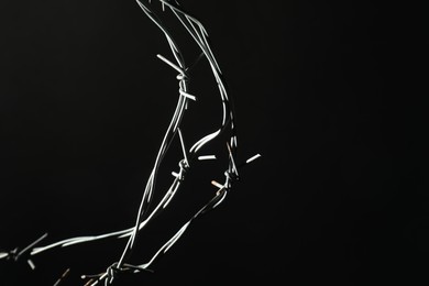 Photo of Metal barbed wire on black background, closeup. Space for text