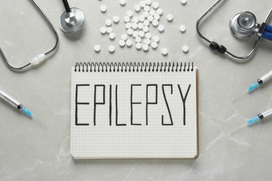 Photo of Notebook with word Epilepsy, stethoscopes, pills and syringes on light grey table, flat lay