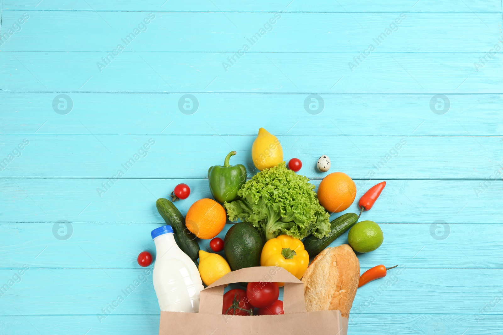 Photo of Flat lay composition with overturned paper bag and groceries on blue wooden background. Space for text